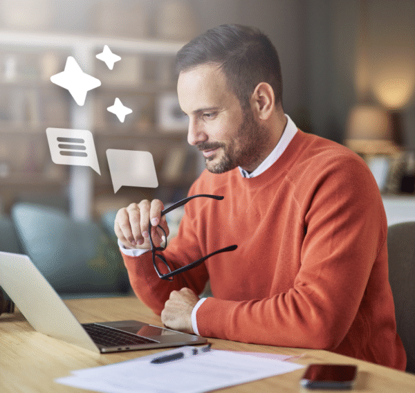 Man in an orange sweater holding glasses while looking at a laptop screen.