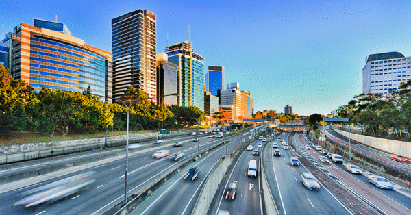 View of a city skyline with modern buildings and a busy highway below during sunset.