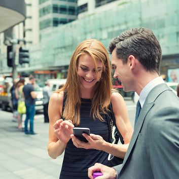 A woman and a man discussing something on a smartphone while standing on a city street.
