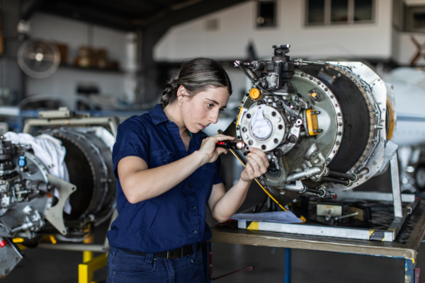 A technician working on an aircraft engine in a hangar setting, focused on the mechanical components.
