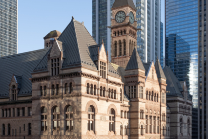 Historic building featuring a clock tower, surrounded by flags and modern skyscrapers.