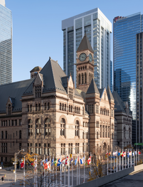 Historic building featuring a clock tower, surrounded by flags and modern skyscrapers.