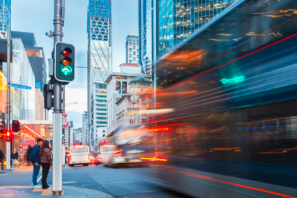 A city intersection featuring traffic lights and a bus in motion amidst tall buildings.