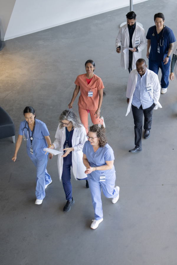 A group of healthcare professionals in scrubs and lab coats walking together in a hospital setting.