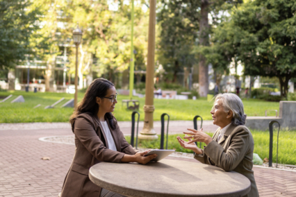 Two women sitting at a round concrete table in a park, engaged in conversation.