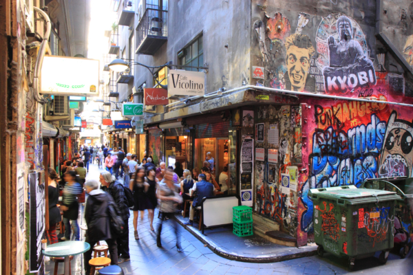 Narrow alleyway featuring street art, cafes, and pedestrians in an urban setting.
