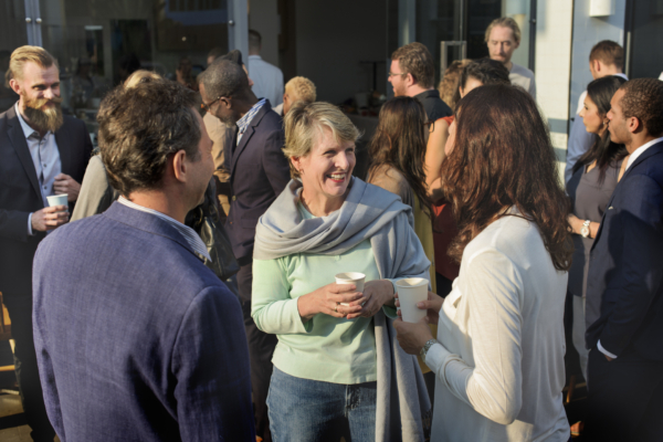 A group of people in business attire engaging in conversation at an event, with some holding cups.