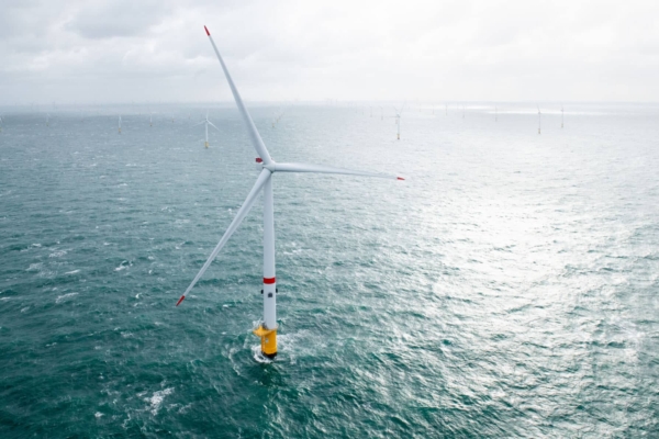 An offshore wind turbine standing in the ocean with multiple turbines visible in the background.