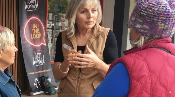 A woman in a vest talking to two individuals outside a store.