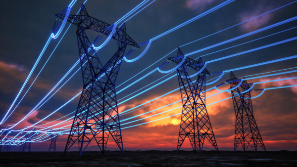 Electric power transmission towers with illuminated lines against a sunset sky.