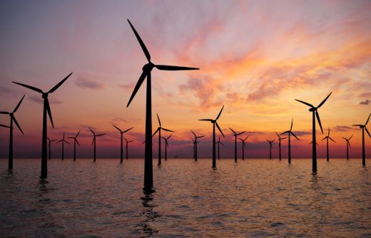 Silhouetted wind turbines standing in water during a colorful sunset.