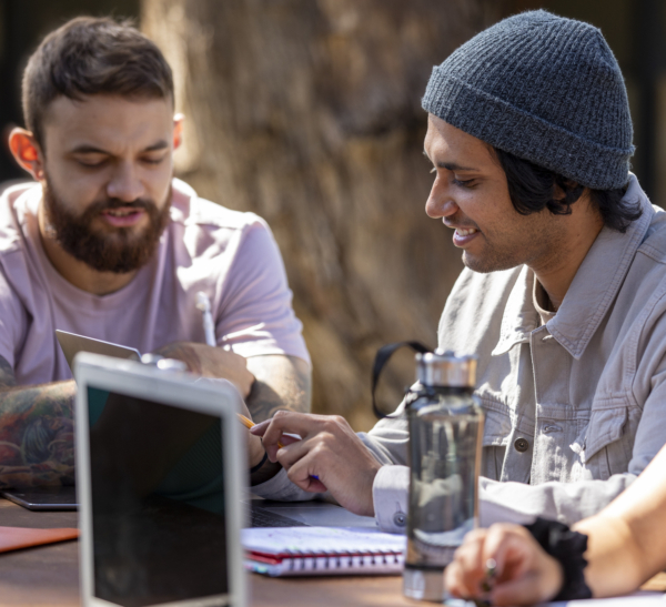Two men discussing over a laptop while seated at a table outdoors.
