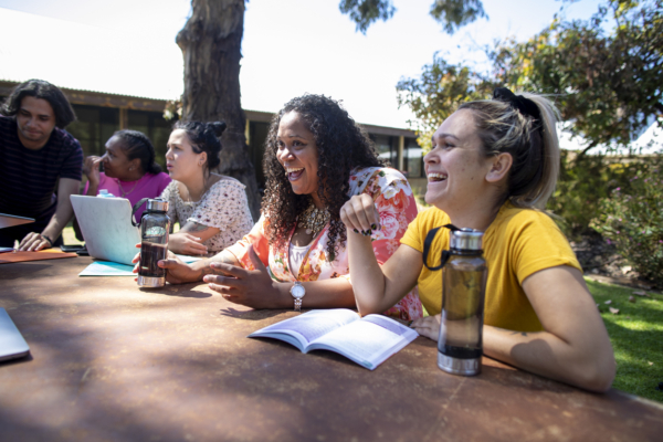 A group of people sitting around a table outdoors, engaged in discussion and laughter.
