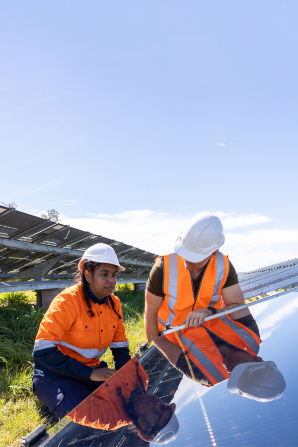 Two workers in safety gear examining a solar panel under a clear blue sky.