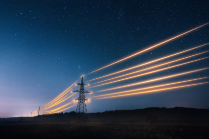 Electric power lines illuminated at night against a starry sky.