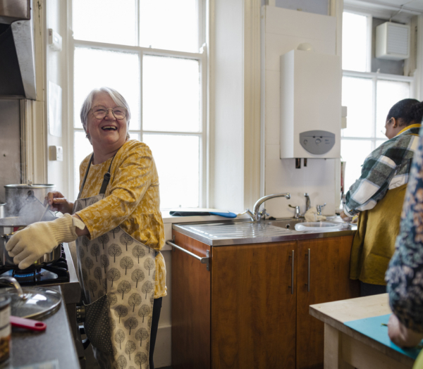 A woman wearing an apron smiles while cooking on a stove in a kitchen.