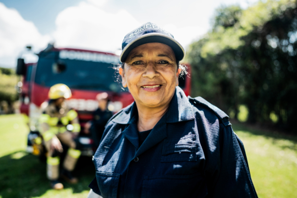 A female firefighter smiling in front of a fire truck with two colleagues in the background.