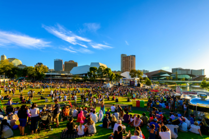 Large crowd gathered in an urban park for a public event with buildings in the background.