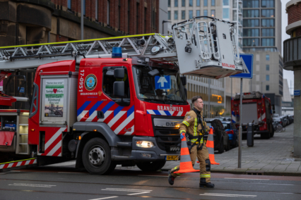 Fire truck with extended ladder and firefighter walking on the street in an urban area.