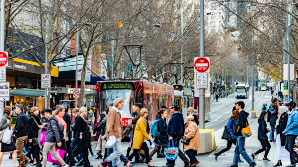 A busy city street with a crowd of pedestrians crossing in front of a tram.