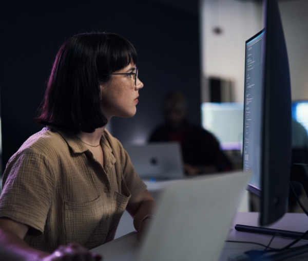 Individual with glasses focused on a computer screen in an office setting.