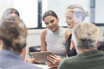 A group of professionals engaged in a meeting, focusing on a tablet being held by one participant.