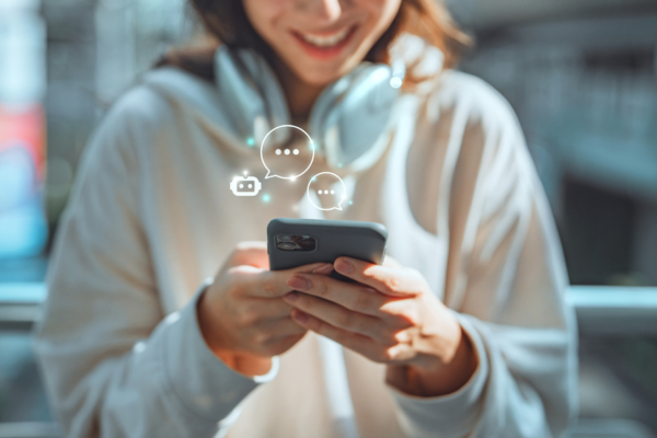 Individual holding a smartphone with headphones around their neck, smiling while interacting with the device.